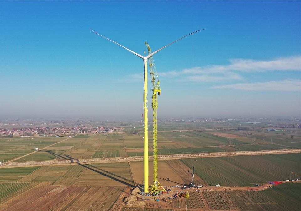 Wind turbine tower crane lifting a turbine blade into position.